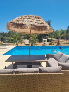 a table with a straw umbrella next to a swimming pool at Villa Das Alfarrobas Eco Design Cabin in Algoz