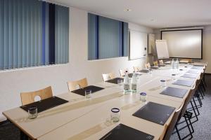 una sala conferenze con tavoli lunghi, sedie e schermo di My Hotel Fribourg a Givisiez