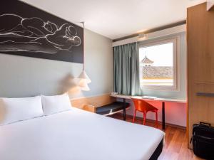 um quarto de hotel com uma cama, uma secretária e uma janela em Ibis Sevilla em Sevilha