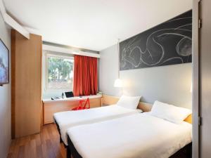 two beds in a hotel room with a window at Ibis Sevilla in Seville