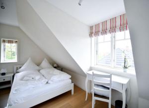 Cette chambre comprend un lit blanc, un bureau et une fenêtre. dans l'établissement Südstrandidyll, à Wyk auf Föhr