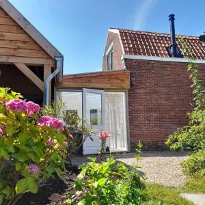 a brick house with a white door and some flowers at Vakantiehuisje Mies Rust en stilte aan het strand in Hoofdplaat