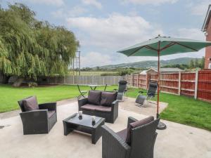 a patio with chairs and an umbrella and a table at Coed Bach in Prestatyn