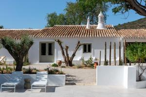 a white house with chairs in front of it at Âmago Guesthouse in Santa Bárbara de Nexe