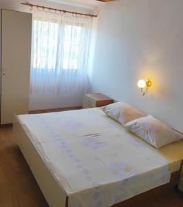 a bedroom with a large white bed with a window at Apartments Lidija in Lopar