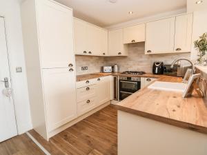 kuchnia z białymi szafkami i drewnianą podłogą w obiekcie 6 Cwrt Griffiths w mieście Rhyl