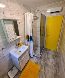 a bathroom with a sink and a shower with a yellow door at Apartman Berlin Sokobanja in Soko Banja
