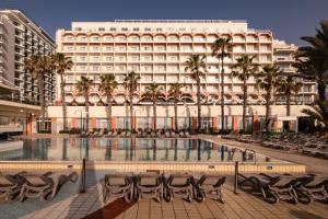 un hotel con sedie e una piscina di fronte a un edificio di QAWRA Palace Resort & SPA a San Pawl il-Baħar