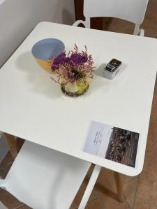 a white table with a bowl of flowers and a book at VILLA DEL COLLE CAMERA MERLOT in Torre del Colle