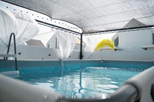a swimming pool with blue water and white curtains at Hayyan cozy place in Kuala Kedah