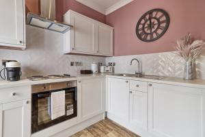 una cocina con armarios blancos y un reloj en la pared en Plush Nest - Charming One-Bedroom Flat - Southend Stays, en Southend-on-Sea