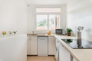 a white kitchen with white cabinets and a window at APPART COSY - COMME À LA MAISON - ST ETIENNE in Saint-Étienne