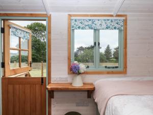 a bedroom with a bed and a window with a vase of flowers at Lottie's Hut in Okehampton