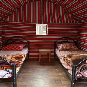 twee bedden in een kamer met een rode streepjesmuur bij Sunset Dreams camp in Wadi Rum