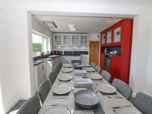 a kitchen with a long table with chairs and a red cabinet at Glanffraw in Aberffraw