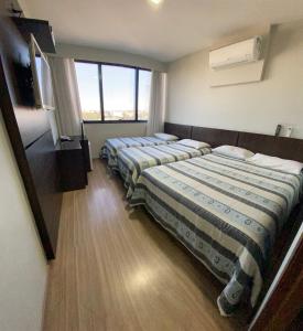 two beds sitting in a room with a window at Hotel Itamaraty in Curitiba