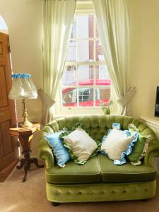 a green couch with pillows on it in front of a window at Traditional 2 bedroom Cottage in Stratford-upon-Avon