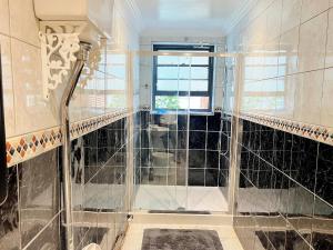 y baño con ducha de cristal y azulejos negros. en Erin Court Mansions - Suite 01, en Croydon
