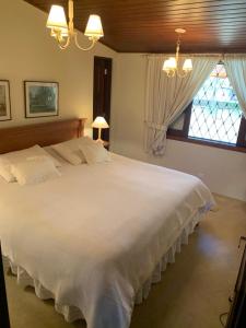 a large white bed in a bedroom with a window at Casa Campos do Jordão, bairro Capivari, Wi-Fi, churrasqueira e forno de pizza, totalmente equipada in Campos do Jordão
