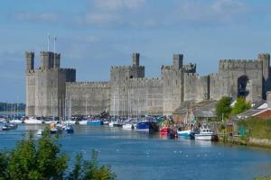 a large castle with boats in a body of water at Charming Cabin near Snowdonia National Park in Caernarfon