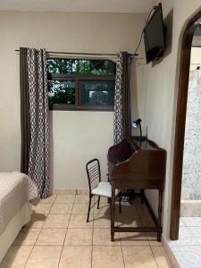 a bedroom with a piano and a chair and a television at El Mesón de los Abuelitos in Retalhuleu