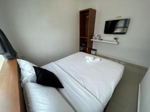 um pequeno quarto com uma cama branca e uma televisão em Pets and Family Guesthouse Kota Laksamana, Melaka em Malaca