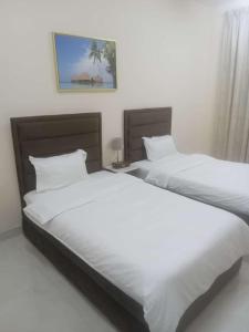 two beds in a bedroom with white sheets at Al Rawda Apartments -Ajman in Ajman 