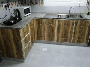 a kitchen with wooden cabinets and a sink and a microwave at Al Rawda Apartments -Ajman in Ajman 