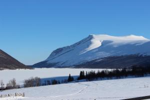 a snow covered mountain in front of a body of water at Mountain cabin Skoldungbu in Vang I Valdres