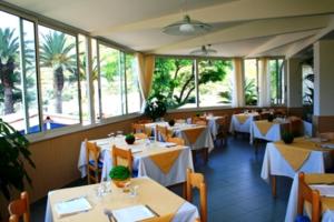 un restaurante con mesas y sillas blancas y ventanas en Sporting Hotel Stella Maris, en Bosa Marina