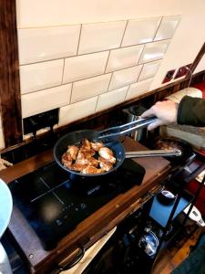 a person cooking food in a pan on a stove at SNUG 30ft NARROWBOAT WITH FIREPLACE in Bishopbriggs