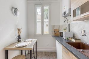 a white kitchen with a table and a microwave at Appartement Moderne, proche Porte de Versailles et Gare de Clamart in Malakoff