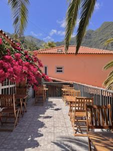 un patio con mesas, sillas y flores rosas en Gardens Guest House en São Vicente