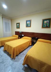 Habitación de hotel con 3 camas con sábanas amarillas en Hostal Restaurante El Lirio en Bollullos par del Condado