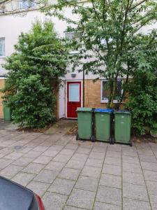 een huis met drie vuilnisbakken en een rode deur bij Curly Curves in North Woolwich