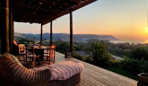 a wooden deck with a table and chairs and the sunset at CORAM DEO SaltyWaves double en-suite rooms with sea views in Coffee Bay
