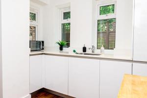a white kitchen with a sink and two windows at Hidden Gem with En-Suites in West Hampstead in London