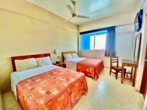 Cette chambre comprend deux lits, une table et une fenêtre. dans l'établissement Hotel Delfines, à Veracruz