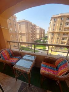 two chairs and a table on a balcony with a view of buildings at شقه في جاردينيا الماظه تحتوى على ٣غرف مكيفه وريسبشن وحمام ومطبخ وريسبشن وبلكونه بجوار سنتر الماظه وسنتر سيتي ستارز الدور الثالث ولها موقع متميز وبلكونه تطل علي مول الكمبوند in Cairo