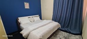 a blue bedroom with a bed with white sheets and pillows at Dinner Bell Lodge in Kitwe