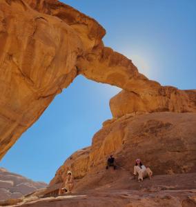 3 Leute sitzen unter einem Bogen in der Wüste in der Unterkunft Travel Wadi Rum in Wadi Rum + 67 Fotos