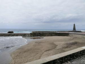 a beach with a lighthouse in the background with the ocean at F&M 'con terraza y tranquilidad' in La Laguna
