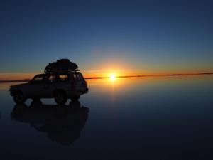 a jeep parked on the beach with the sun setting at HOSTAL SALARCITO in Uyuni