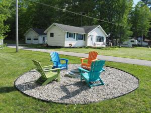four colorful chairs sitting on a circle in the grass at Manist-easy - Lakefront With Dock And Kayaks! in Kalkaska