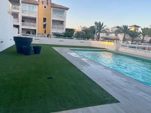 einem Pool mit grünem Gras an der Seite eines Gebäudes in der Unterkunft TERRAZA LA MARINA in Elche