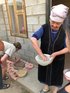 Eine Frau, die eine Schüssel Essen hält, während eine andere Frau Essen zubereitet. in der Unterkunft Song Kol Flex Travel guests house in Dzhangyaryk