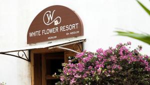 ein Schild für ein Restaurant mit weißen Blumen in einem Gebäude mit lila Blumen in der Unterkunft Whiteflower Resort Morjim in Morjim