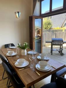 a wooden table with plates and glasses on it at Stylish contemporary seaside holiday home with 5 bedrooms, sea view, parking and EV point in Kent