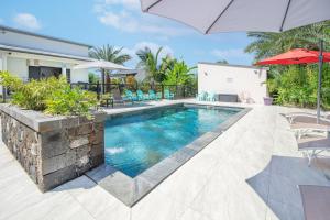 a pool with chairs and umbrellas next to a house at Ô Ruisseau Lodges - Lodge Cocotier in Saint-Louis