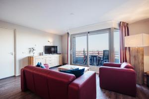 una sala de estar con 2 muebles de color rojo y una gran ventana en Appartementen Hotel Meyer, en Bergen aan Zee